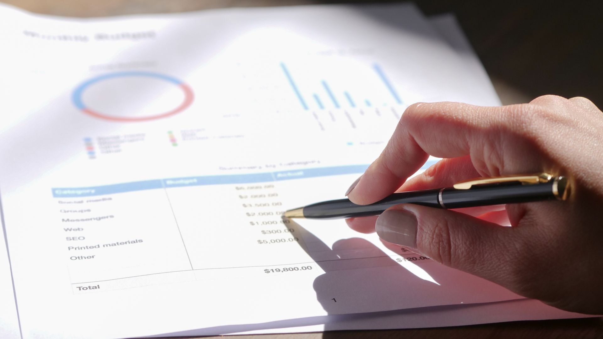 A hand reviewing a financial report with a pen